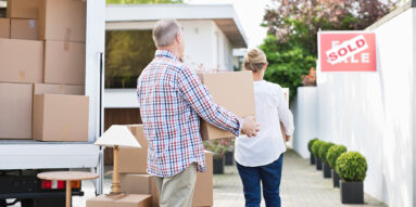 Couple unloading boxes from moving van, sold sign