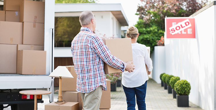 Couple unloading boxes from moving van, sold sign